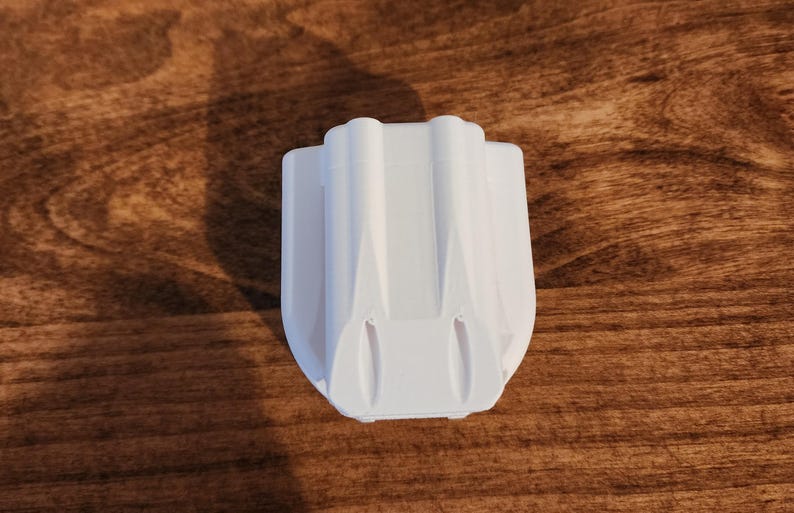 May include: A white, 3D-printed object with a unique, symmetrical design. The object has a rectangular base and a series of vertical, curved ridges. The item is sitting on a wooden surface.