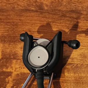 May include: A black and silver stethoscope with a gray diaphragm and black earpieces. The stethoscope is positioned against a wooden surface, with the focus on the chest piece and earpieces.