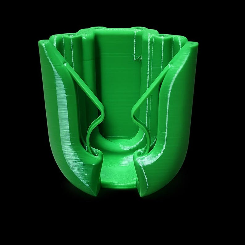 May include: A bright green, 3D-printed cup holder with a unique design. The holder features curved arms that extend from the base, creating a secure grip. The cup holder is made of a solid, smooth material and is designed to hold a standard-sized cup.