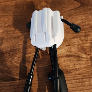 May include: A white plastic device with a rectangular body and two black arms extending downwards. The device has a textured surface and is set against a wooden background. The arms have black, rounded ends.