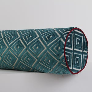 Peut inclure: Un coussin traversin cylindrique présentant un motif géométrique en losanges bleu sarcelle et blanc. Le tissu a un aspect texturé et les extrémités circulaires sont finies avec un fin passepoil rouge foncé soulignant la forme cylindrique.