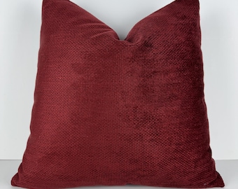 Può includere: Un cuscino decorativo quadrato color bordeaux. Il cuscino ha un aspetto strutturato e tessuto e un aspetto morbido e soffice. Il cuscino è di colore pieno e viene probabilmente utilizzato per l'arredamento della casa.