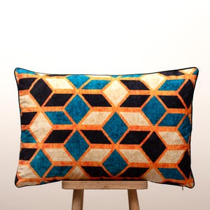 Può includere: Cuscino rettangolare decorativo con motivo geometrico. Il design presenta forme a diamante nei colori verde acqua, nero, arancione e crema. Il cuscino ha un bordo nero ed è appoggiato su uno sgabello di legno.