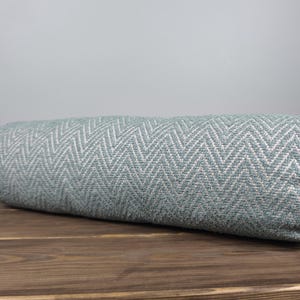 Capa de almofada cilíndrica com estampa chevron em tons de azul-petróleo: Almofada lombar em linho e algodão.