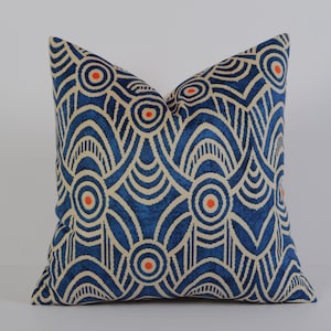 Könnte beinhalten: Ein quadratisches Zierkissen mit einem blauen und cremefarbenen geometrischen Muster. Das Design zeigt konzentrische Kreise mit orangefarbenen Zentren und geschwungenen Linien. Das Kissen ist ein Einrichtungsgegenstand.