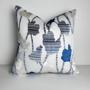 May include: A square cushion featuring a floral design in white, navy, and grey. The pattern includes stylized flowers and striped elements. The cushion is designed for decorative use, adding a touch of style to any living space.