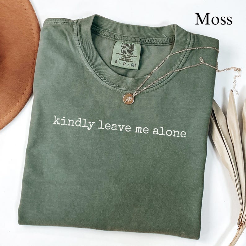 Green t-shirt with "kindly leave me alone" text and a gold necklace.