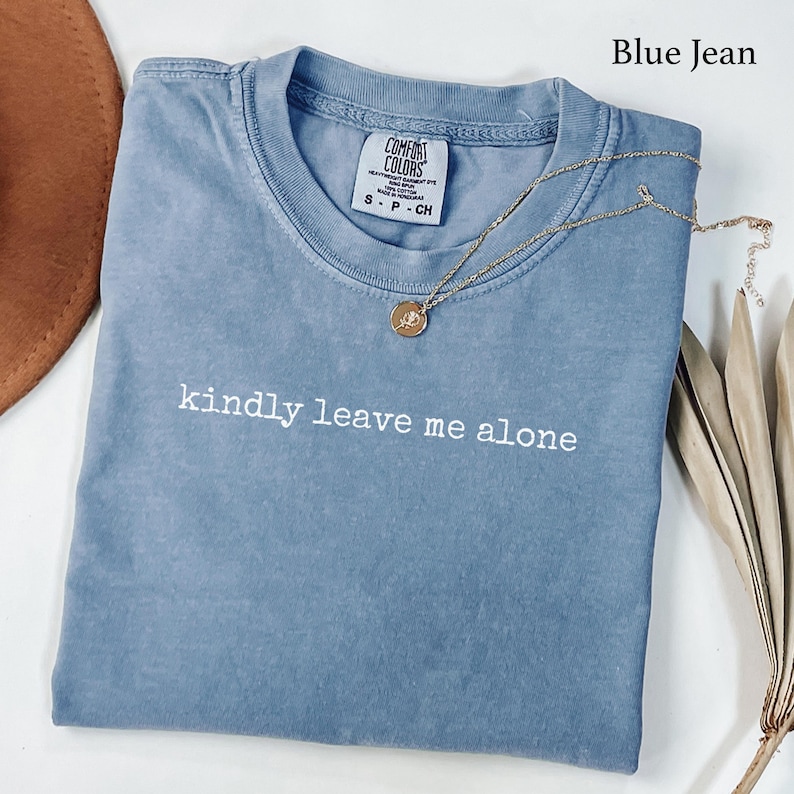 Blue t-shirt with "kindly leave me alone" text and a gold necklace.