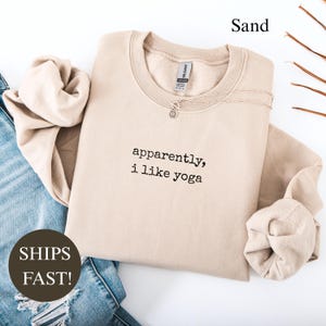Sand colored crewneck sweatshirt with "apparently, i like yoga" printed on it.