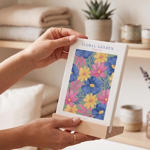 Könnte beinhalten: Ein floraler Kunstdruck mit einem Muster aus blauen, rosa und gelben Blumen auf hellgrünem Hintergrund. Der Druck wird in einem Holzständer präsentiert. Der Text "FLORAL GARDEN" und "keep growing" ist oben aufgedruckt.