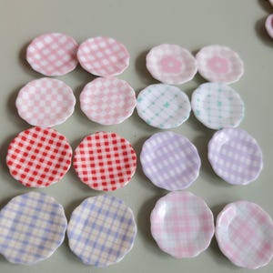 Puede incluir: Una colección de platos decorativos en miniatura en varios colores y patrones. Los platos presentan diseños de cuadros y florales en tonos de rosa, rojo, morado, azul y verde. Estos pequeños platos son ideales para casas de muñecas o proyectos de manualidades.