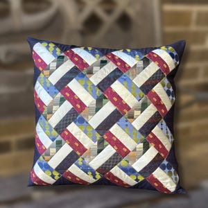 May include: A square throw pillow featuring a woven pattern made from various neckties. The design incorporates strips of fabric in shades of deep red, cream, navy blue, and lime green, with diverse geometric and polka dot prints throughout the surface.