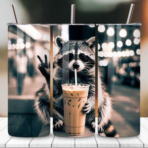 May include: A stainless steel tumbler featuring a raccoon wearing sunglasses and drinking iced coffee with a straw. The raccoon is making a peace sign with its left hand. The background is a blurred street scene with bokeh lights.