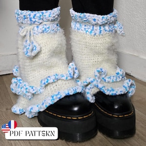 May include: A pair of white crochet boot cuffs with blue accents and a ruffled edge. The cuffs are worn over black boots. The image includes the text "PDF PATTERN" with the American and French flags.