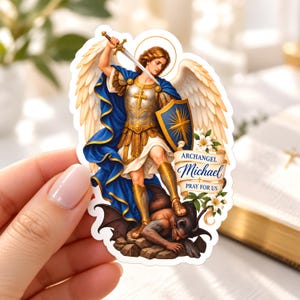 Peut inclure: Un autocollant découpé représentant l'archange Michel avec de grandes ailes blanches, portant une armure dorée et une cape bleue, tenant une épée et un bouclier au-dessus d'une figure sombre. Une bannière indique Archangel Michael Pray For Us.