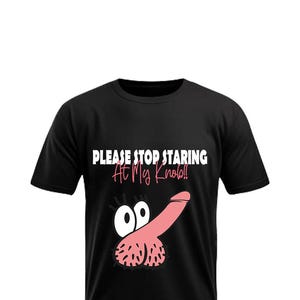 May include: Black t-shirt with a humorous graphic of a pink cartoon penis with eyes and the text "PLEASE STOP STARING AT My Knob!!" in white and pink. The shirt is a crew neck.