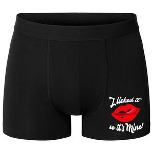 May include: Black boxer shorts featuring a red lip graphic and the text "I licked it so it's Mine!" on the front. The shorts have a black elasticated waistband and a traditional boxer short design.