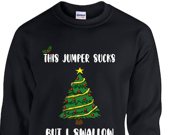 Peut inclure: Sweat-shirt noir avec le texte "THIS JUMPER SUCKS BUT I SWALLOW" et un sapin de Noël. L'arbre est vert avec des boules rouges et une étoile jaune. Une branche de houx est en haut.