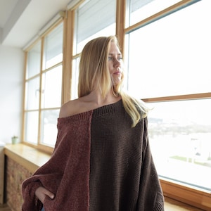 May include: A woman wearing a brown and burgundy knitted sweater with a relaxed fit. The sweater has a unique color block design and is made of a soft, comfortable material.