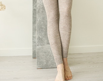 May include: A pair of brown knitted leggings with a subtle flecked texture. The leggings are being worn by a person with bare feet.