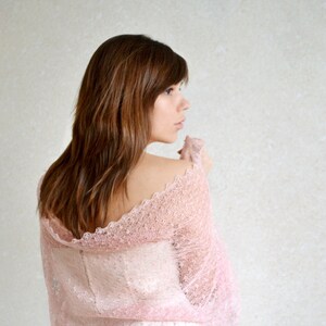 May include: A woman wearing a delicate pink lace shawl with a scalloped edge. The shawl is sheer and lightweight, and it drapes beautifully over her shoulders.