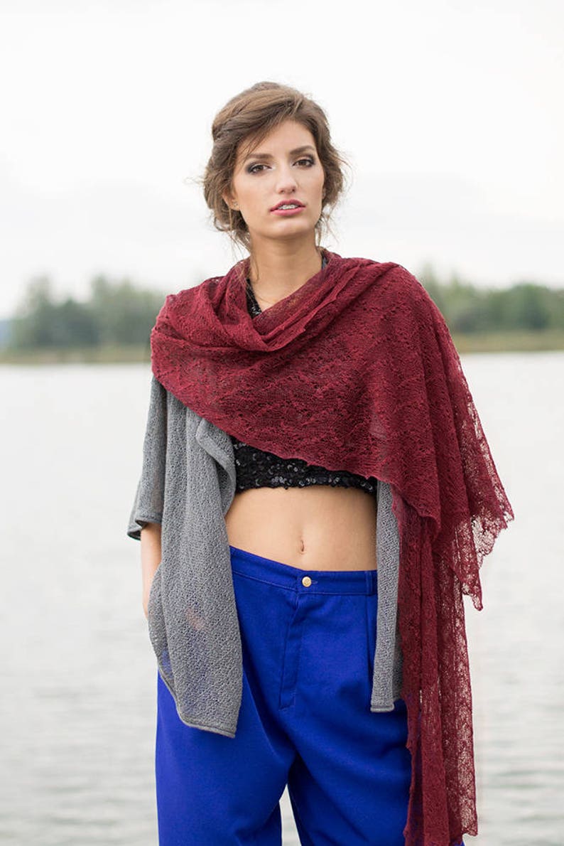 Peut inclure: Une femme portant un cardigan gris, un pantalon bleu et un ch&acirc;le en dentelle bordeaux. Le ch&acirc;le est drap&eacute; autour de son cou et de ses &eacute;paules.