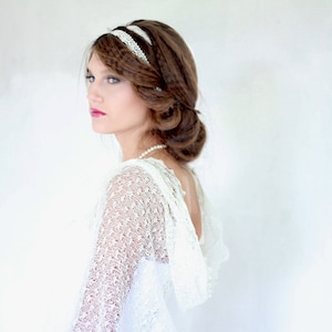 May include: A woman with long brown hair wearing a white lace dress and a white lace headband. She is looking to the side and has a soft smile on her face.