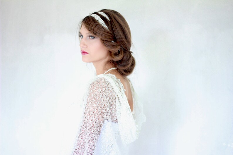 May include: A woman with long brown hair wearing a white lace dress and a white lace headband. She is looking to the side and has a soft smile on her face.