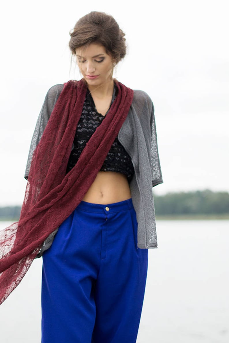 Peut inclure: Une femme portant une &eacute;charpe en dentelle bordeaux, un cardigan gris, un haut en dentelle noire et un pantalon bleu.