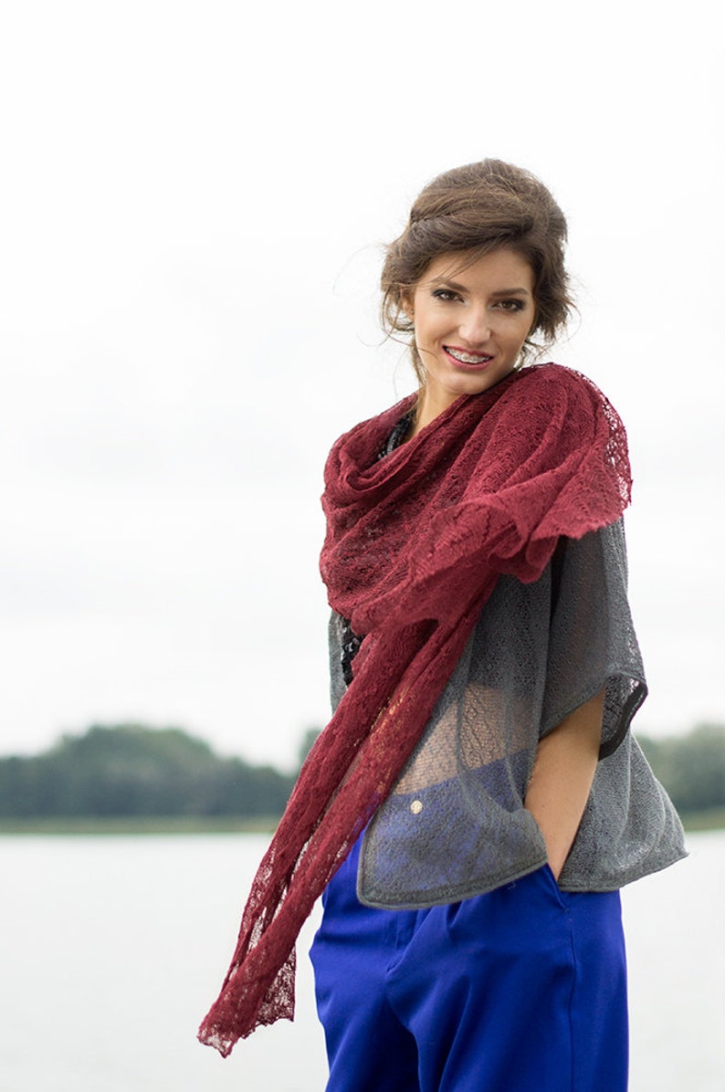 Peut inclure: Une femme portant un haut gris avec une &eacute;charpe en dentelle rouge, un pantalon bleu et un collier en or. Elle sourit et regarde la cam&eacute;ra.