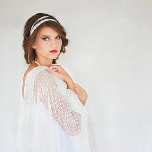 May include: A woman with short brown hair wearing a white lace shawl and a silver headband. She is looking at the camera with a serious expression.