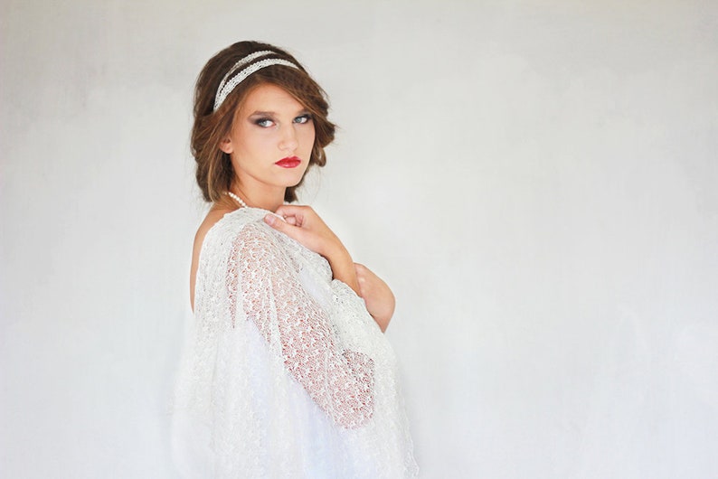 May include: A woman with short brown hair wearing a white lace shawl and a silver headband. She is looking at the camera with a serious expression.