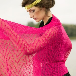May include: A woman wearing a pink lace shawl with a gold sequined headband. The shawl is draped over her shoulders and she is looking down.