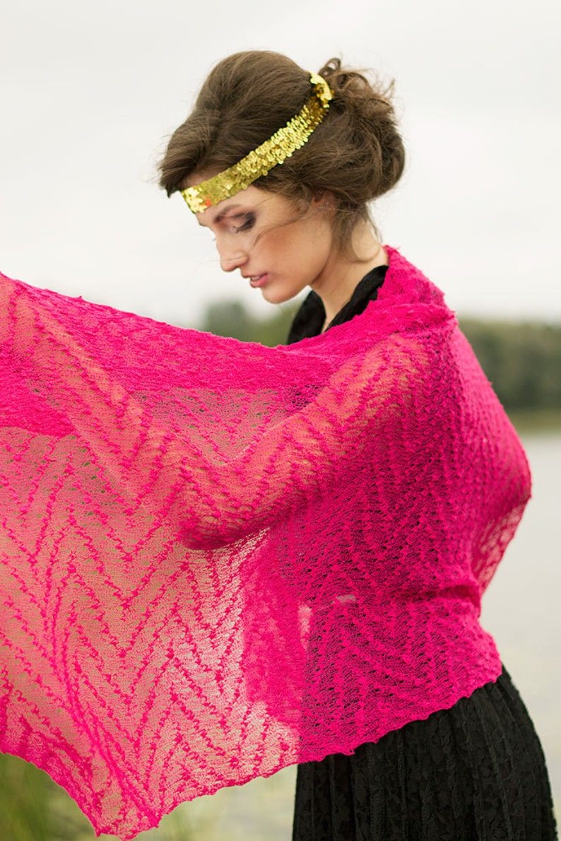 May include: A woman wearing a pink lace shawl with a gold sequined headband. The shawl is draped over her shoulders and she is looking down.