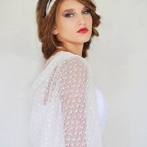 May include: A woman wearing a white lace shawl with a beaded headband. She has brown hair and is wearing red lipstick.