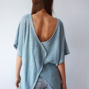 K&ouml;nnte beinhalten: Ein hellblaues Strickoberteil mit tiefem R&uuml;cken und einem Kreuzdesign im R&uuml;cken. Das Oberteil ist locker geschnitten und hat eine lockere Silhouette.