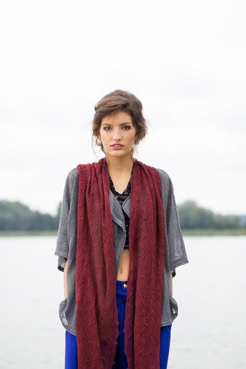 Peut inclure: Une femme portant un cardigan en tricot gris avec une &eacute;charpe en dentelle bordeaux, un jean bleu et un haut noir.