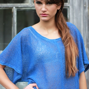 May include: A blue, short-sleeved top with a scoop neck. The top has a loose, flowing fit and is made of a sheer, textured fabric. The model is wearing the top with her hand on her hip.