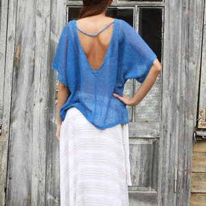 May include: A blue open-back top with short sleeves and a deep V-neck. The top is paired with a long, white and light brown striped skirt. The clothing is worn in front of a weathered wooden door.