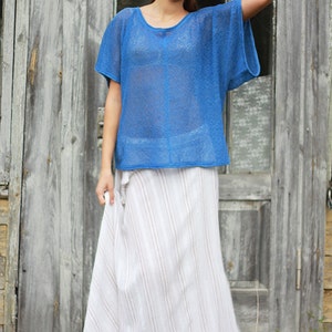 May include: A woman's outfit featuring a sheer, short-sleeved, royal blue top and a long, flowing white skirt with vertical stripes. The clothing is lightweight and appears suitable for warm weather. The background is a weathered wooden door.
