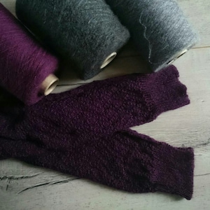 Puede incluir: Dos ovillos de lana, uno morado y otro gris, y una tela de punto morado con un patr&oacute;n texturizado.