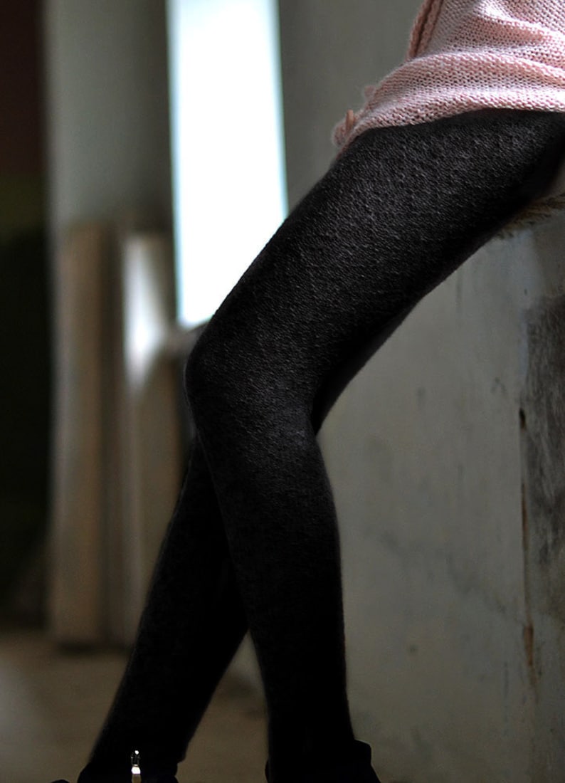 Puede incluir: Un par de medias negras con un patr&oacute;n texturizado. Las medias las lleva una persona de pie cerca de una pared.