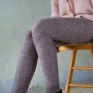 Puede incluir: Una mujer con un c&aacute;rdigan de punto rosa y medias marrones con estampado est&aacute; sentada en una silla de madera. Lleva botas negras de cordones con detalles dorados.