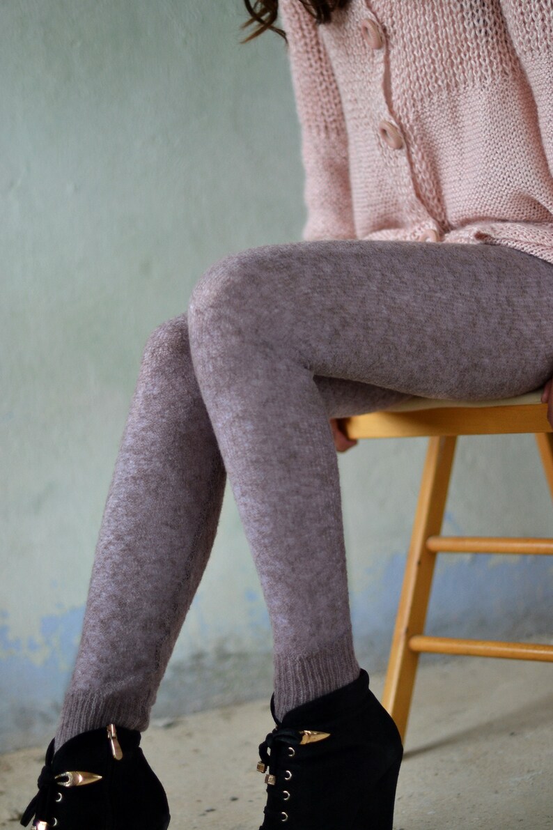 Puede incluir: Una mujer con un c&aacute;rdigan de punto rosa y medias marrones con estampado est&aacute; sentada en una silla de madera. Lleva botas negras de cordones con detalles dorados.