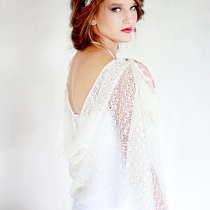 May include: A white lace bridal shawl with a delicate pattern. The shawl is draped over the shoulders of a person wearing a white dress.