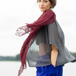 Peut inclure: Une femme portant un haut en tricot gris avec un ch&acirc;le en dentelle bordeaux. Elle porte un pantalon bleu et a les cheveux tir&eacute;s en arri&egrave;re.