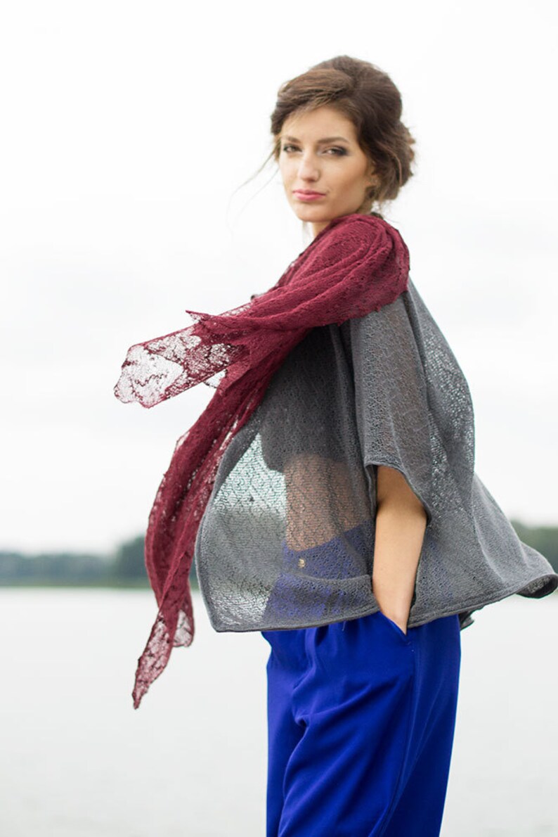 Peut inclure: Une femme portant un haut en tricot gris avec un ch&acirc;le en dentelle bordeaux. Elle porte un pantalon bleu et a les cheveux tir&eacute;s en arri&egrave;re.