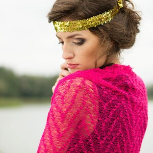 May include: A woman with brown hair wearing a pink lace shawl and a gold sequined headband.