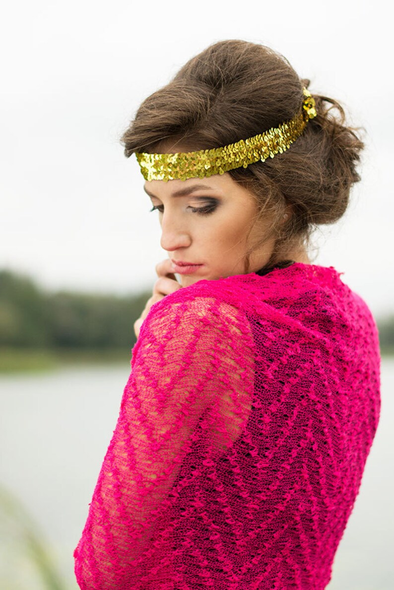 May include: A woman with brown hair wearing a pink lace shawl and a gold sequined headband.