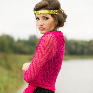 May include: A woman wearing a pink lace shawl over a black dress. She is wearing a gold headband and has her hair pulled back.
